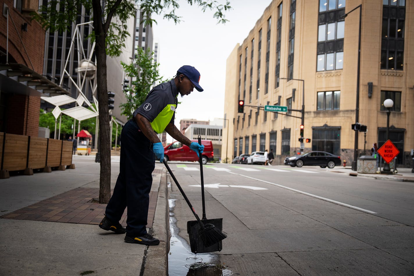 A man in uniform uses a broom and dustpan to collect garbage on the street.